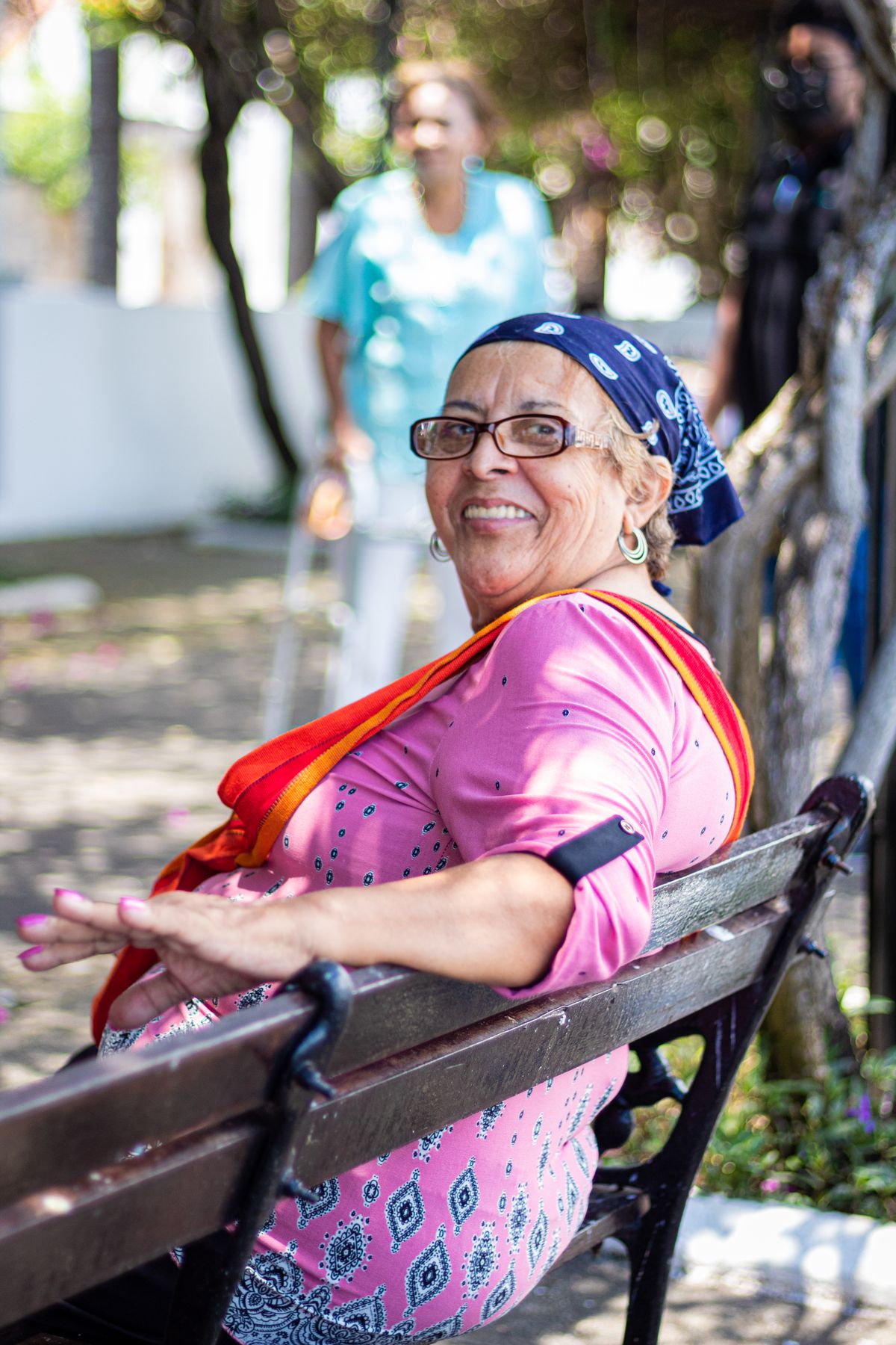 Senhora sorrindo sentada em um banco de praça